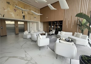 Un vestíbulo moderno con piso de mármol, sofás blancos, una mesa de centro y una estantería.