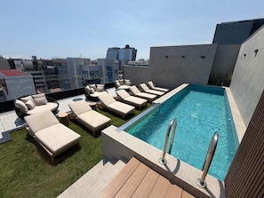 Un área de piscina en la azotea con sillones de descanso y una piscina.