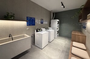 A modern laundry room with a built-in washing machine, a drying machine, and a sink. There are informational posters on the wall and a potted plant on the left.