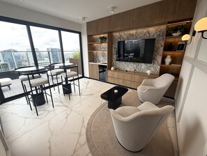 Una sala de estar moderna con un televisor grande, asientos cómodos, un comedor y vistas a la ciudad.