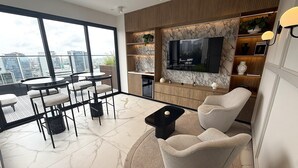 Un salon moderne doté d’un grand téléviseur, de sièges confortables, d’un coin repas et offrant une vue sur le paysage urbain.