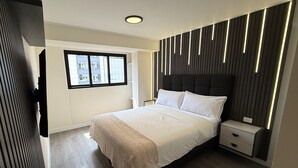 Une chambre moderne avec un grand lit, des tables de chevet, une fenêtre et une vue sur les bâtiments environnants.