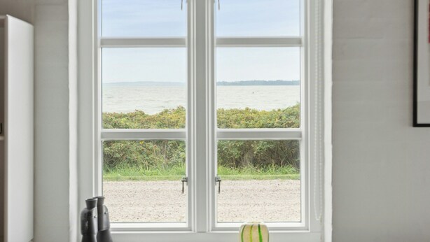 A room with a large window overlooking a body of water and a grassy area.