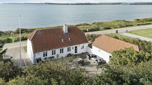 A white building with a red-tiled roof, a flagpole, and a view of a large body of water.