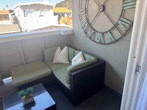 Ein Balkon mit einer Couch, einem kleinen Tisch mit einer Pflanze und einer großen Wanduhr.