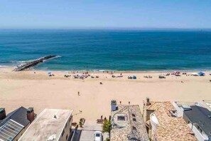 Una playa con un rompeolas rocoso, orilla arenosa y edificios con tejados de tejas.