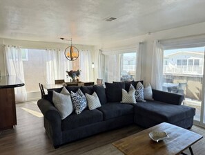 Ein modernes Wohnzimmer mit einem Ecksofa, einem Esstisch und großen Fenstern.