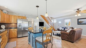 A spacious kitchen with a central island, wooden cabinets, a refrigerator, and a dining area with a chair and table. - Spacious 5-bedroom WAVES OF HAMPTON I & II Combined (Hampton)