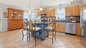A kitchen with wooden cabinets, a central island with chairs, a stainless steel refrigerator, and pendant lighting. - Spacious 5-bedroom WAVES OF HAMPTON I & II Combined (Hampton)