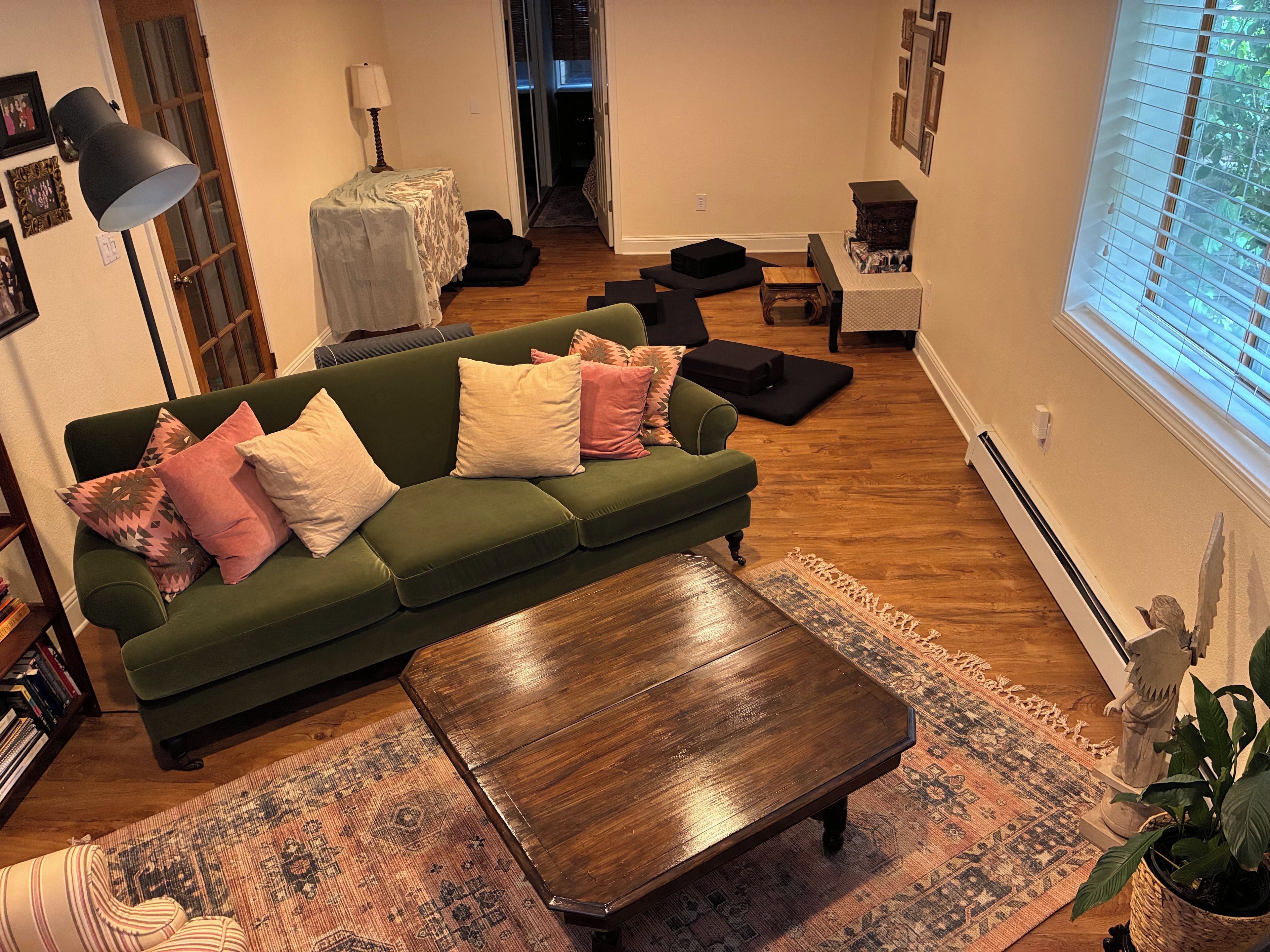 Un canapé vert avec des coussins, une table basse en bois, un tapis à motifs, une lampe et une statue.