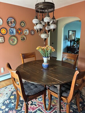Un coin repas comprenant une table ronde en bois, six chaises, un vase avec des fleurs et un luminaire décoratif au plafond.