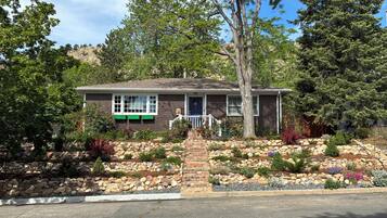 A two-story house with a stone foundation, a front porch, and a well-maintained garden with various plants and a small tree.