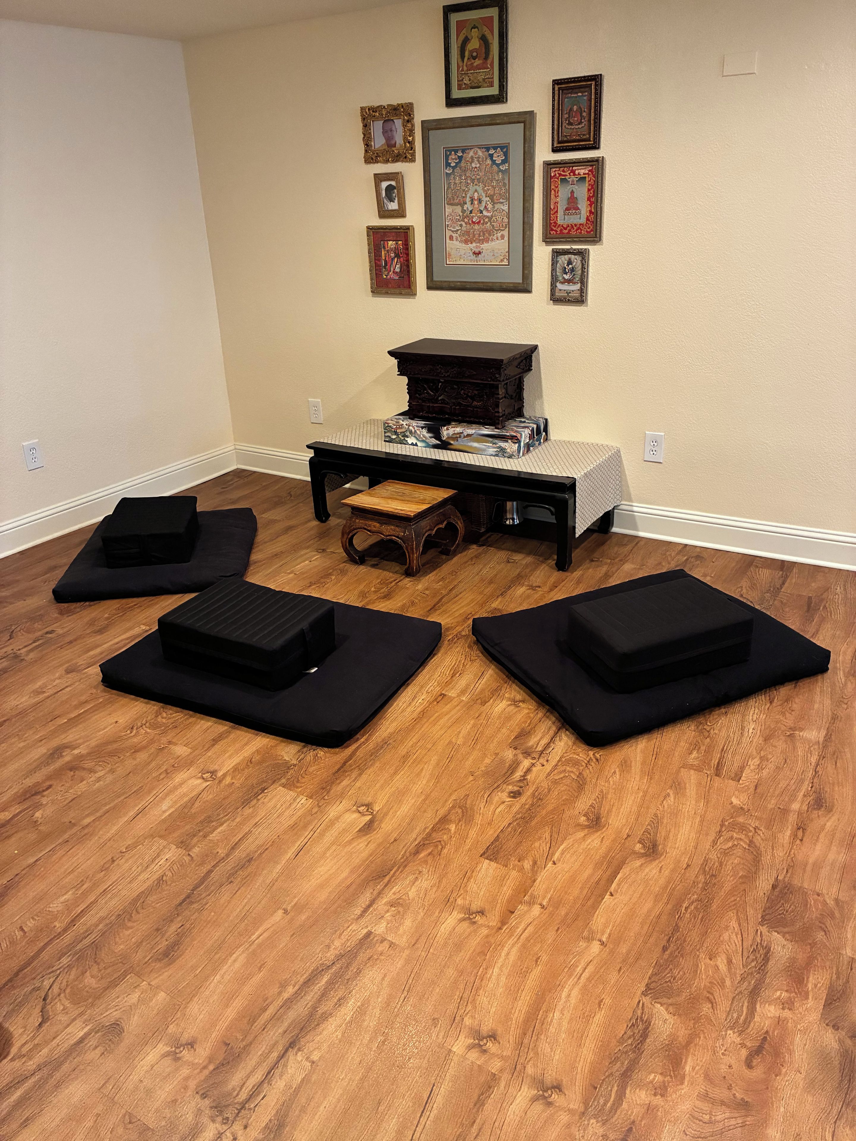 A room with a wooden floor, a black table with a patterned tablecloth, and four black cushions arranged in a semi-circle.