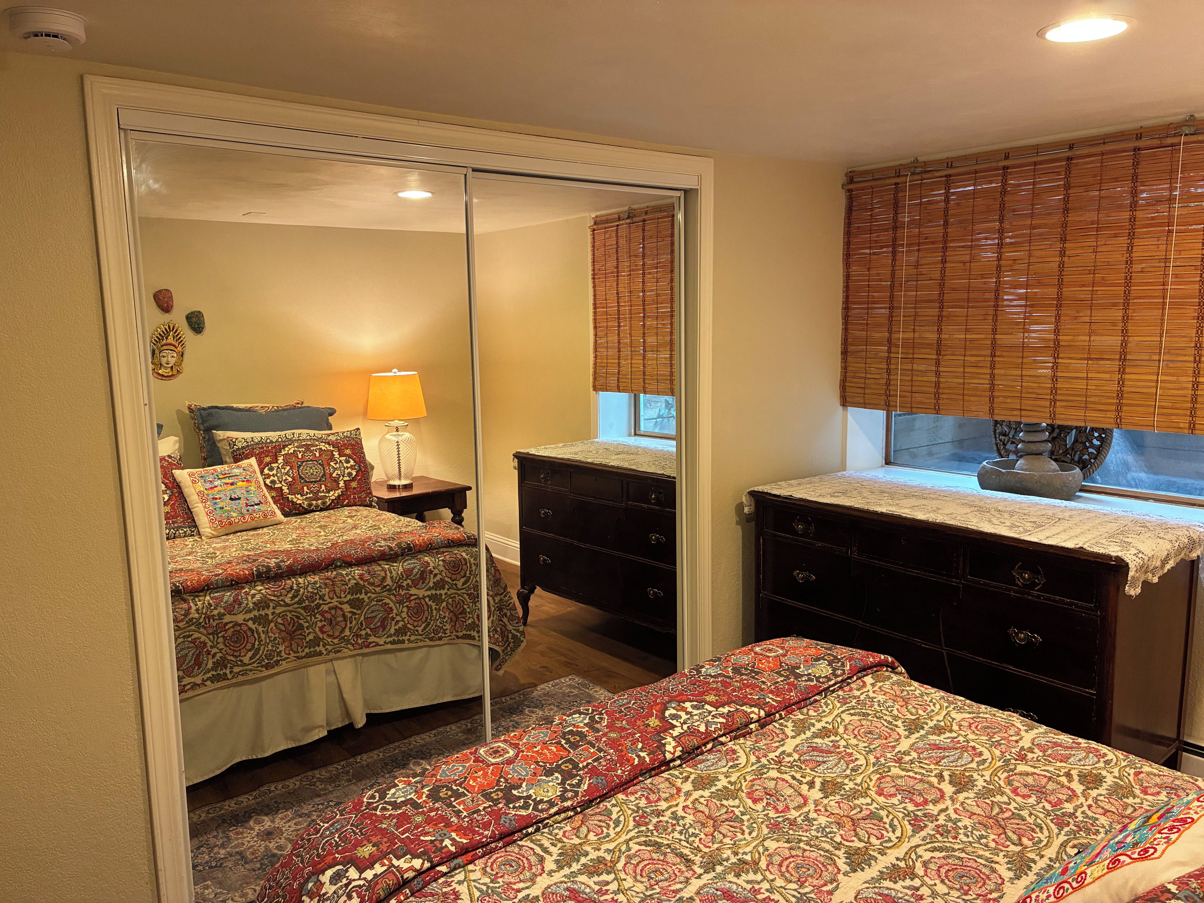 Une chambre à coucher avec un lit, une commode, un miroir et une fenêtre avec des stores.
