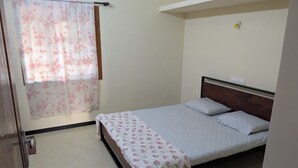 Ein Schlafzimmer mit einem Bett, einem Fenster mit floralem Vorhang, einer Steckdose und einer Tür.