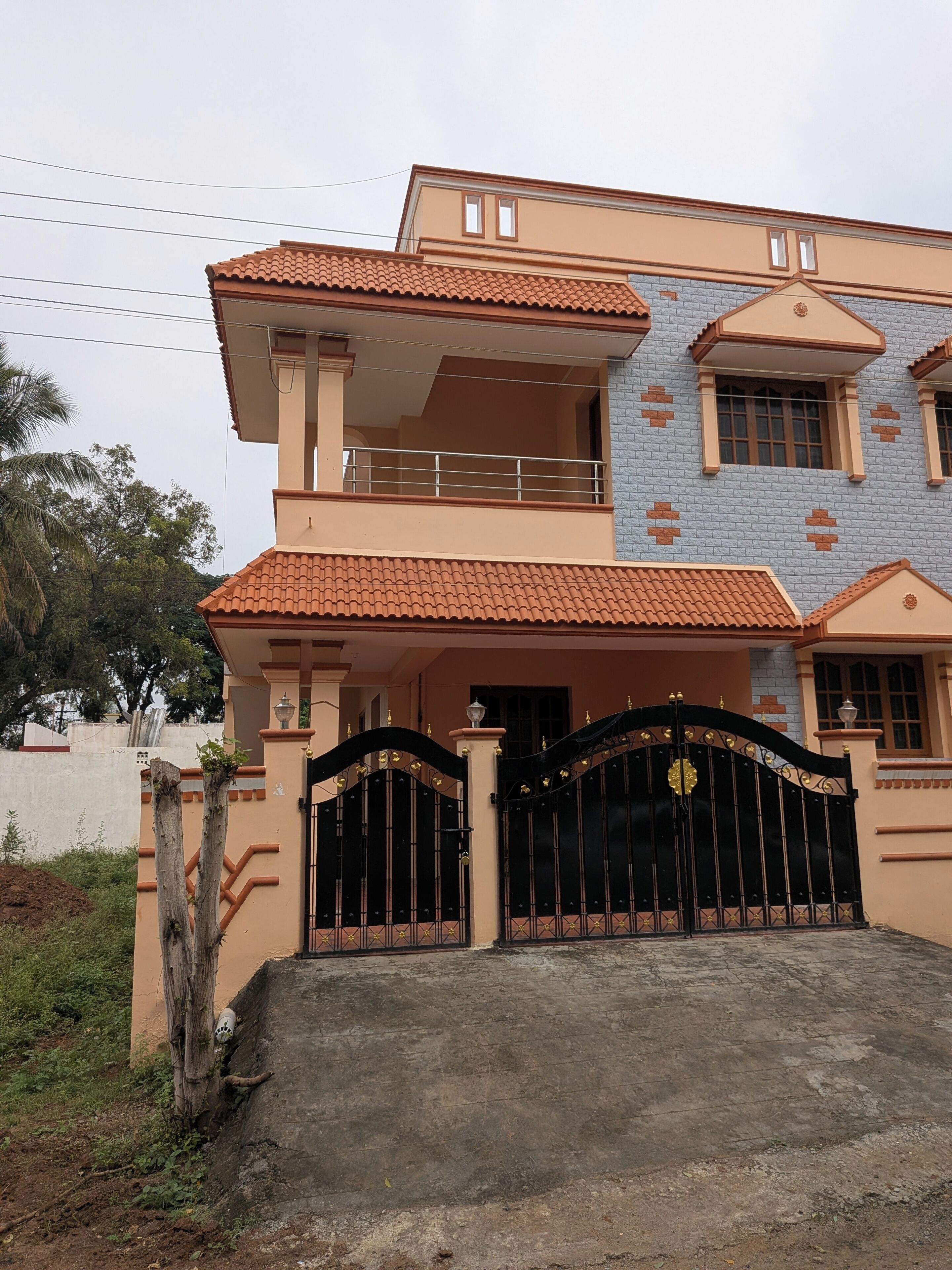 Uma casa de dois andares com varanda, portão fechado e entrada por calçada de concreto.