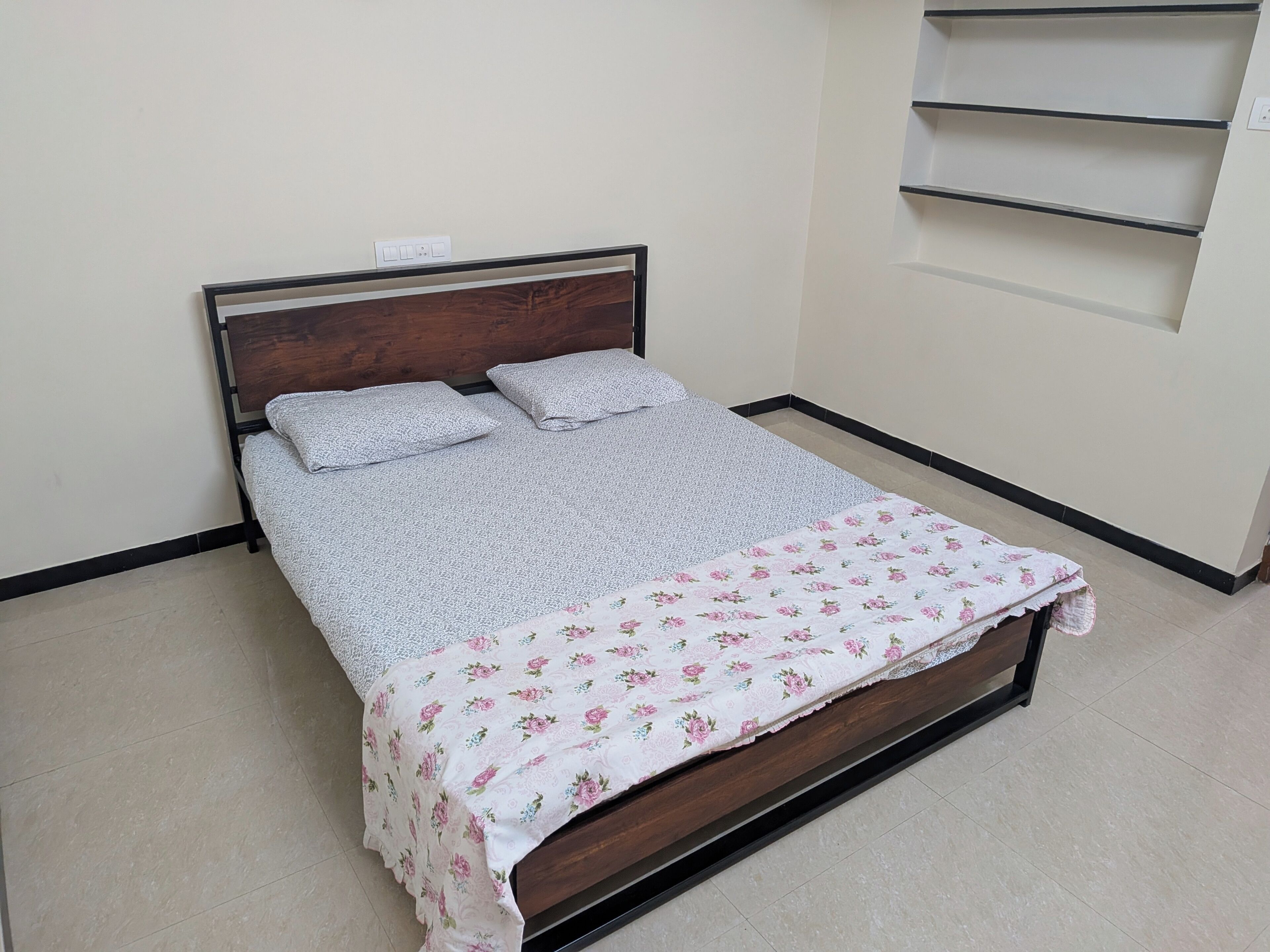 Uma cama com cabeceira de madeira, cobre floral e um edredom cinza simples.