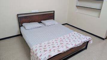 Uma cama com cabeceira de madeira, cobre floral e um edredom cinza simples.