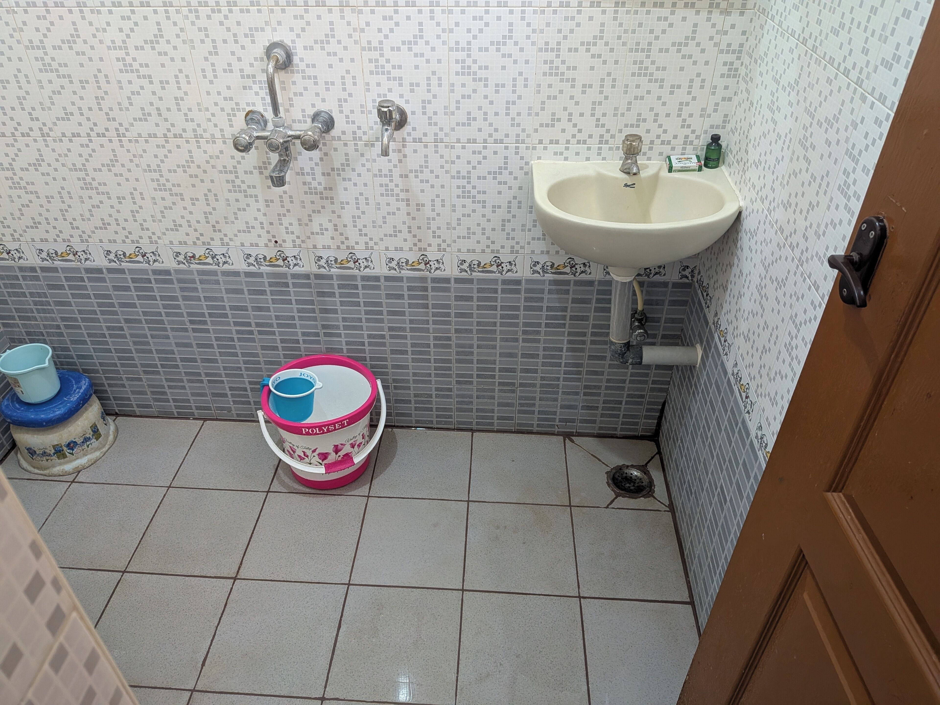 A bathroom with a tiled floor, a sink, a toilet, and a shower with a faucet.