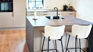 A modern kitchen with a central island, bar stools, a built-in oven, and a window. - Newly renovated holiday home near HimmerLand (Farsø)