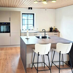 A modern kitchen with a central island, bar stools, a built-in oven, and a window. - Newly renovated holiday home near HimmerLand (Farsø)