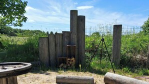 A rustic outdoor setting with a fire pit, wooden logs, and a metal grill. - Newly renovated holiday home near HimmerLand (Farsø)