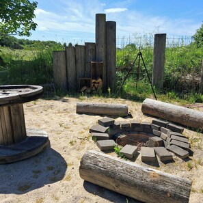 Un espace extérieur rustique avec un foyer, des bûches de bois et un barbecue en métal.