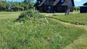 A large, dark-colored house with a sloped roof, a balcony, and a well-maintained lawn. - Newly renovated holiday home near HimmerLand (Farsø)