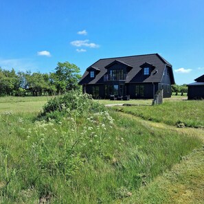 A large, dark-colored house with a sloped roof, a balcony, and a well-maintained lawn. - Newly renovated holiday home near HimmerLand (Farsø)