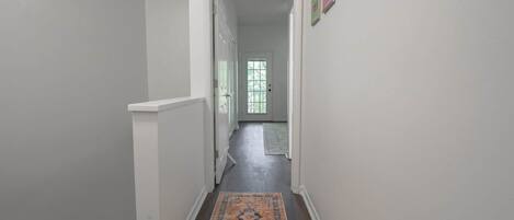 A hallway with a patterned rug, white walls, and a door leading to another room.