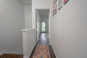 A hallway with a patterned rug, white walls, and a door leading to another room. - Eagles Landing-easy access to AU (Auburn)