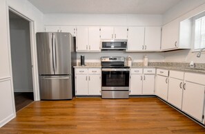 A modern kitchen with stainless steel appliances, white cabinetry, and a wooden floor. - Eagles Landing-easy access to AU (Auburn)