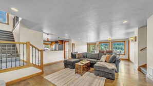 Amplia sala de estar con escalera, un conjunto de sofás y vistas al exterior.