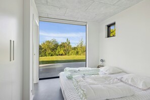 A bedroom with a large sliding glass door leading to a view of a green landscape. - Summer house with sea view high in Handrup (Ebeltoft)