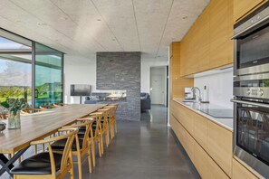 A modern kitchen with a large island, stainless steel appliances, and a dining area with a long table and chairs. - Summer house with sea view high in Handrup (Ebeltoft)