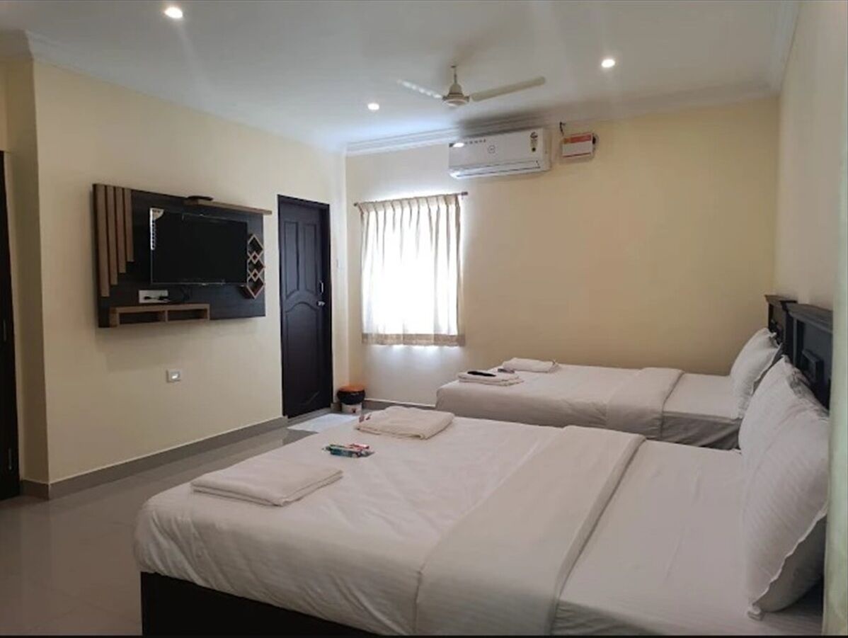 Una habitación de hotel con dos camas, un televisor montado en la pared, un aire acondicionado y un ventilador de techo.