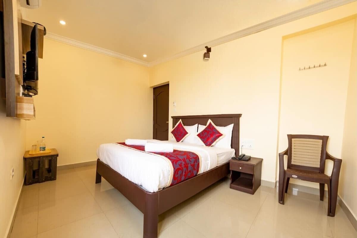 A hotel room with a bed, bedside table, chair, and a wall-mounted TV.