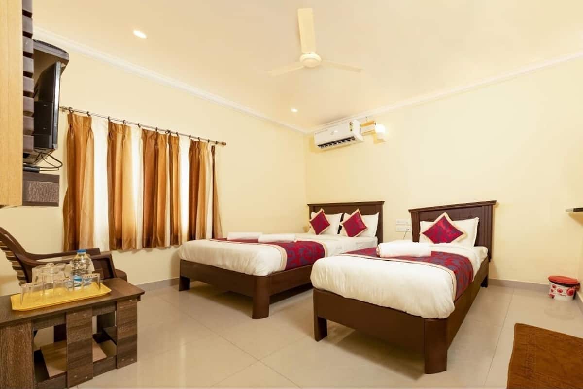 A hotel room with two beds, a desk with a tray, a ceiling fan, and an air conditioning unit.