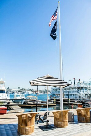 Ein Yachthafen mit vertäuten Booten, eine Fahnenstange mit der US-amerikanischen Flagge und Sitzgelegenheiten im Freien mit einem Streifenverdeck.
