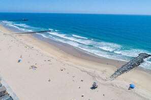Ein Strand mit einem Steg, der sich ins Meer erstreckt, feinem Sand und einem Rettungsturm.