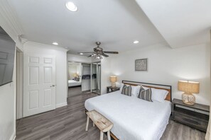 Ein Schlafzimmer mit Bett, Nachttischen, Deckenventilator und einer Tür zu einem anderen Raum.