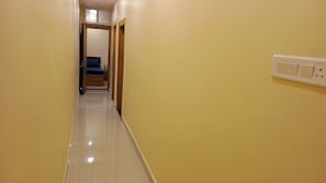 A narrow hallway with a bed in the background, a door on the left, and a wall socket on the right. - Hotel Mahakal Ujjain Prime  (Ujjain)