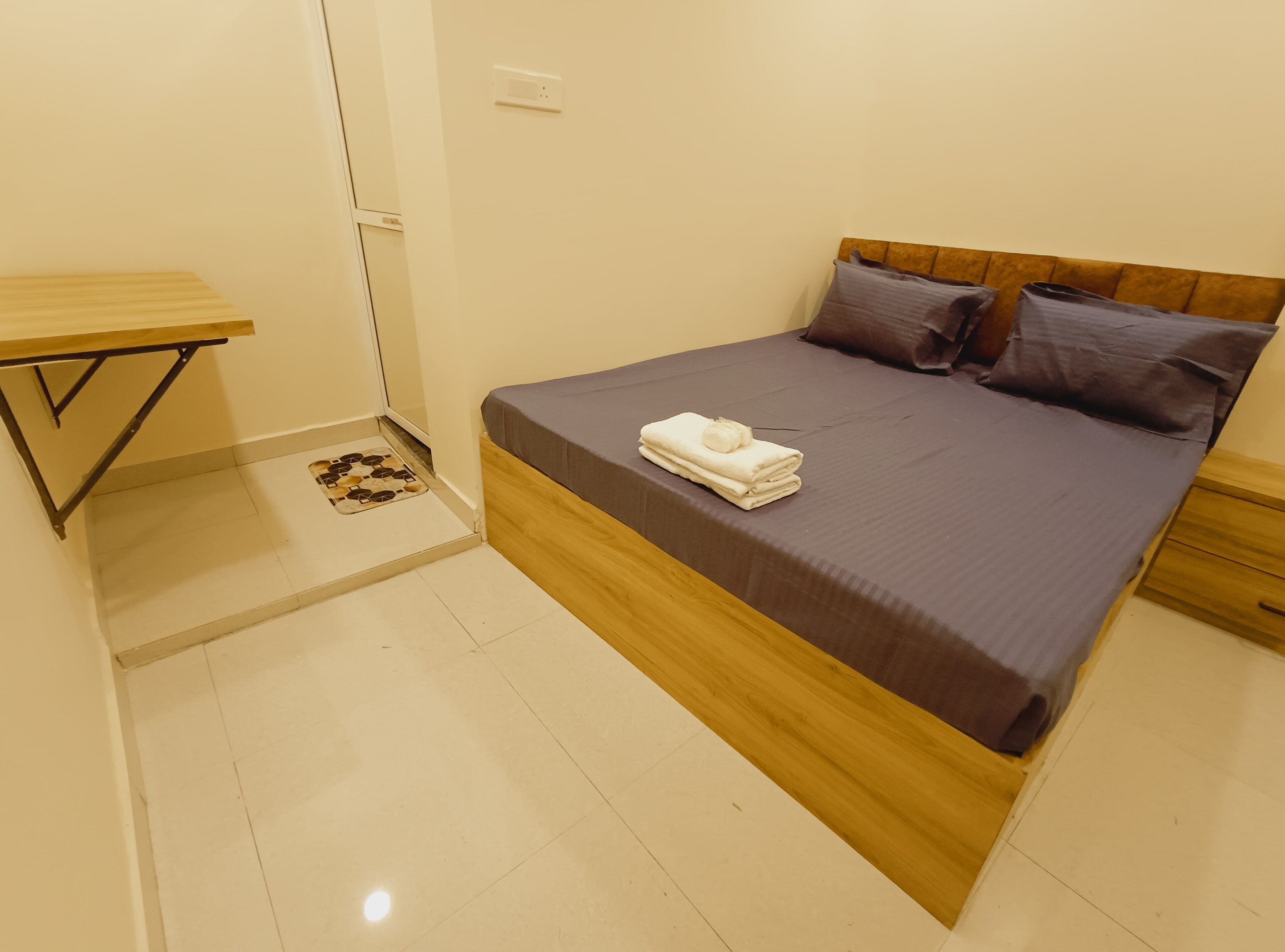 Une chambre à coucher avec un lit, des oreillers, une table de chevet et un petit tabouret en bois.