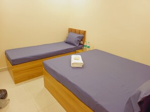 A room with two wooden beds, each with a purple mattress and matching pillows. A folded white towel is placed on one bed. - Hotel Mahakal Ujjain Prime  (Ujjain)