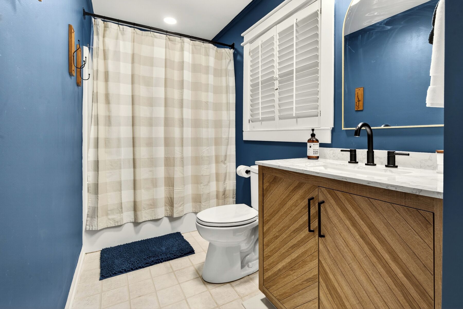 Een badkamer met toilet, wastafel met spiegel, douchegordijn en raam met jaloezieën.