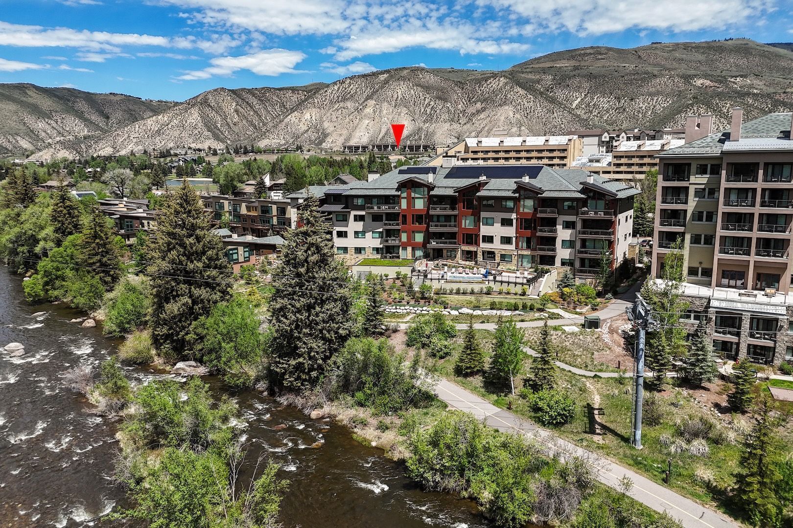 A riverside hotel with modern architecture, a central courtyard, and a mountain backdrop.