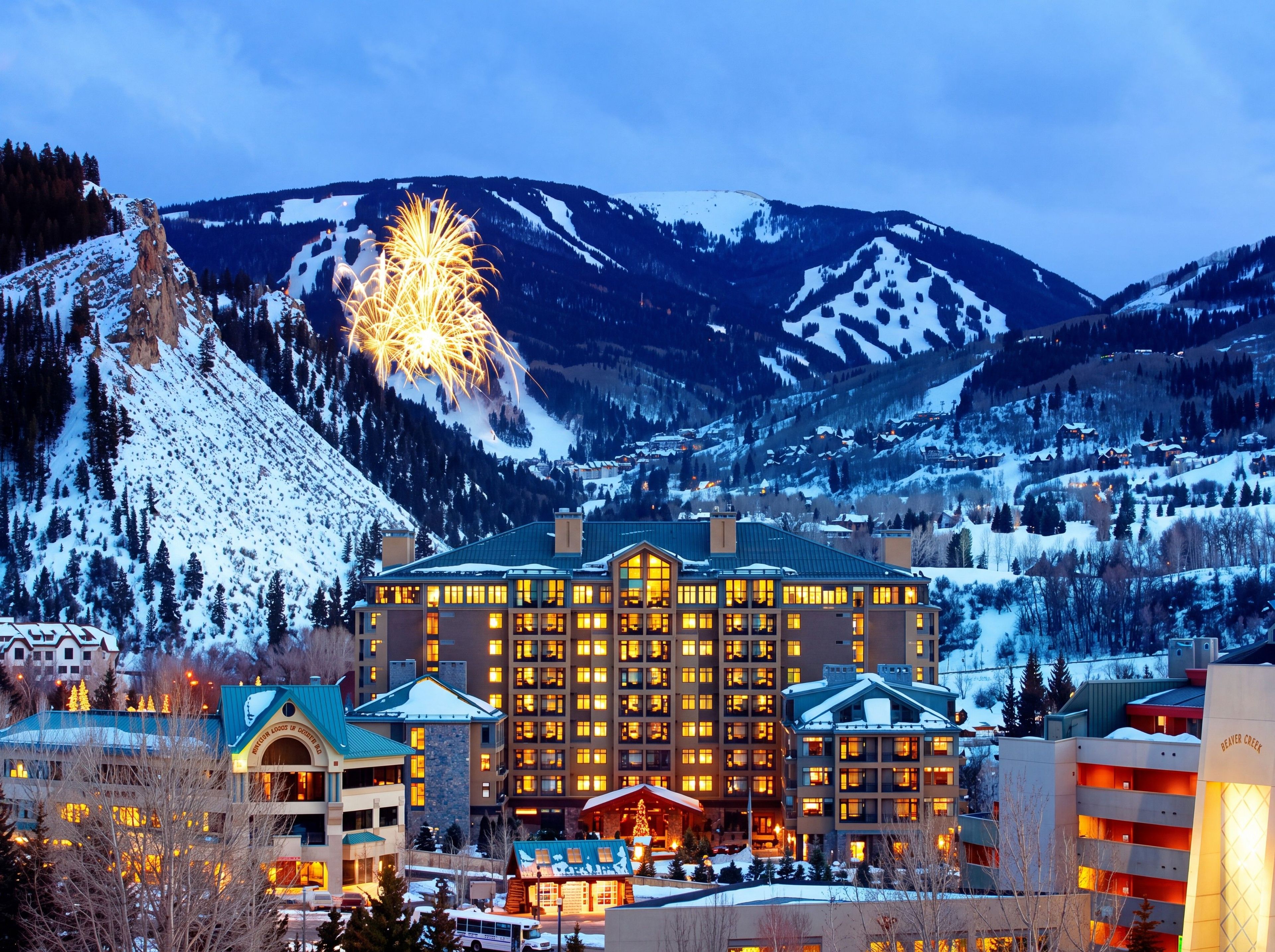 A hotel with multiple floors, a ski resort in the background, and a mountain range.