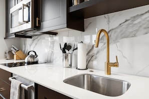 Eine moderne Küche mit einer Spüle aus Edelstahl, einem Wasserhahn in Goldoptik und einer Marmor-Spritzschutzwand.