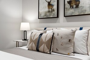 A neatly made bed with patterned pillows, a bedside table with a lamp, and two framed animal paintings on the wall. - Upscale Riverfront Condo- BC Gondola, Dog Friendly (Avon)
