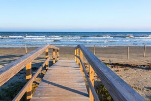 Une promenade en bois qui mène à une plage, avec des vagues en arrière-plan.